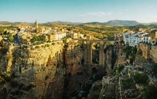 Artistic illustration depicting the cliffside city of Ronda, Spain, perched along the sheer vertical drops of the El Tajo Gorge with a dramatic stone bridge.