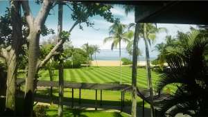 A manicured green striped lawn framed by palm trees leading to a sandy beach and ocean at Shangri-La Rasa Ria in Tuaran.