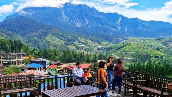 Visitors enjoying the panoramic view of Mount Kinabalu and Kundasang valley from a wooden outdoor terrace.