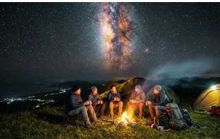 Hikers camping around a campfire beneath the Milky Way at the summit ridge of Bukit Bongol in Kota Belud.