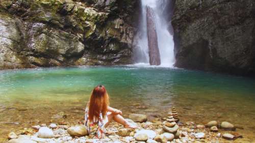 A woman sitting by a stacked stone cairn in front of the turquoise pool and cascading Murug-Turug waterfall.